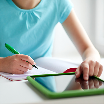 Student writing in a notebook and using a tablet